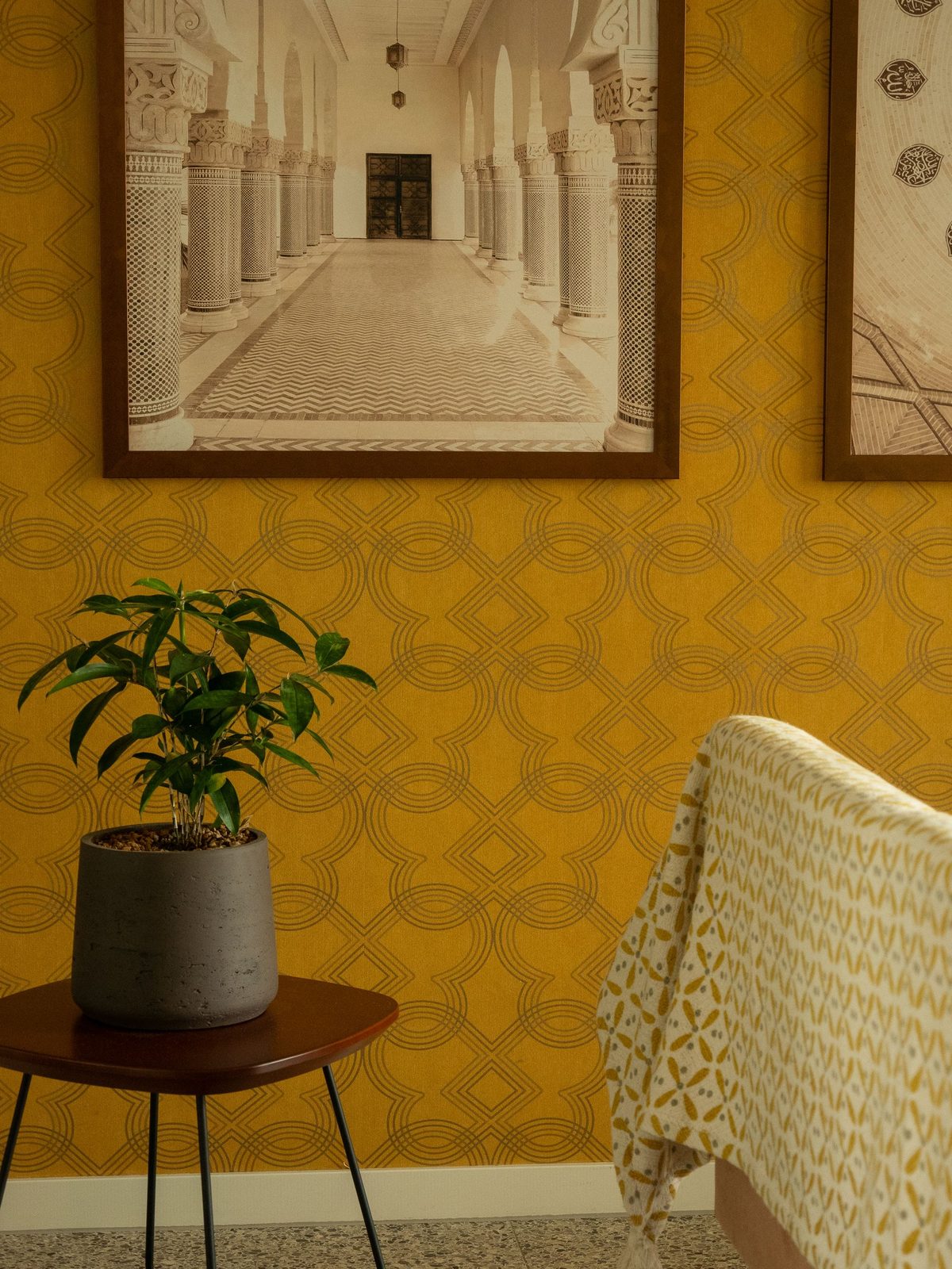 Reading nook with warm mustard-yellow patterned wallpaper, framed art and a potted plant