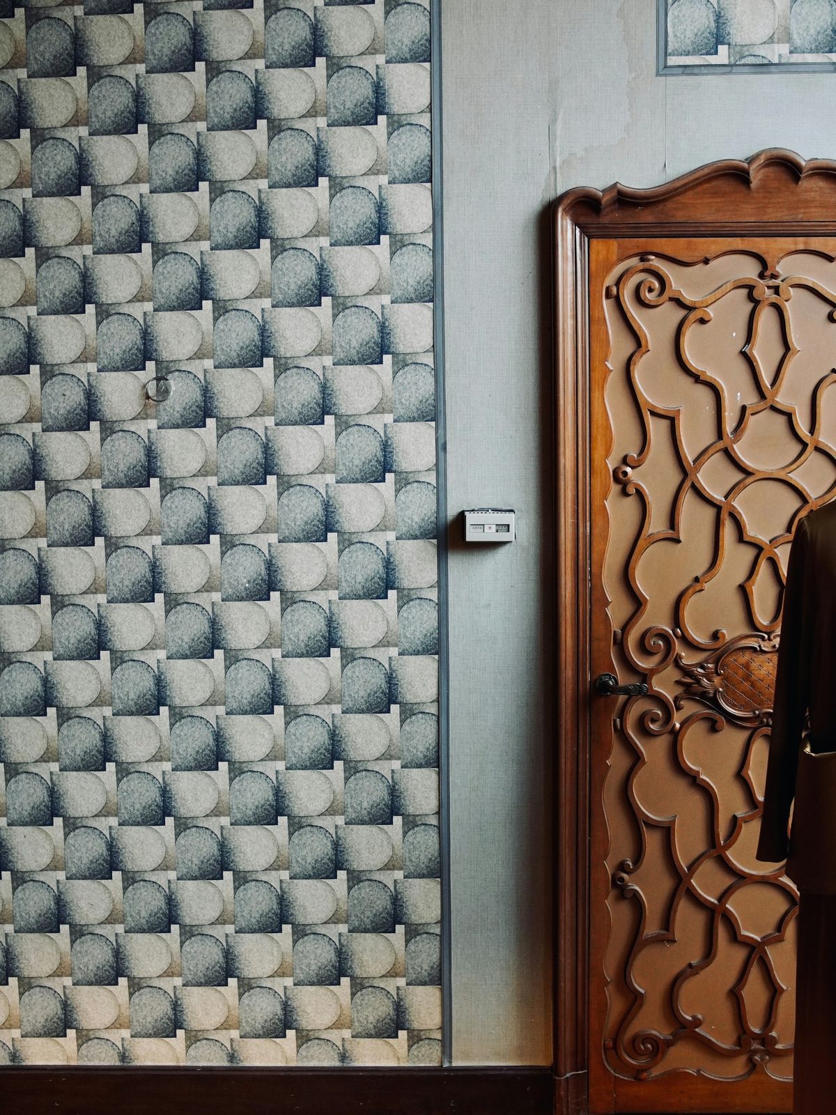 Powder-room wall in teal geometric wallpaper next to a carved wood door